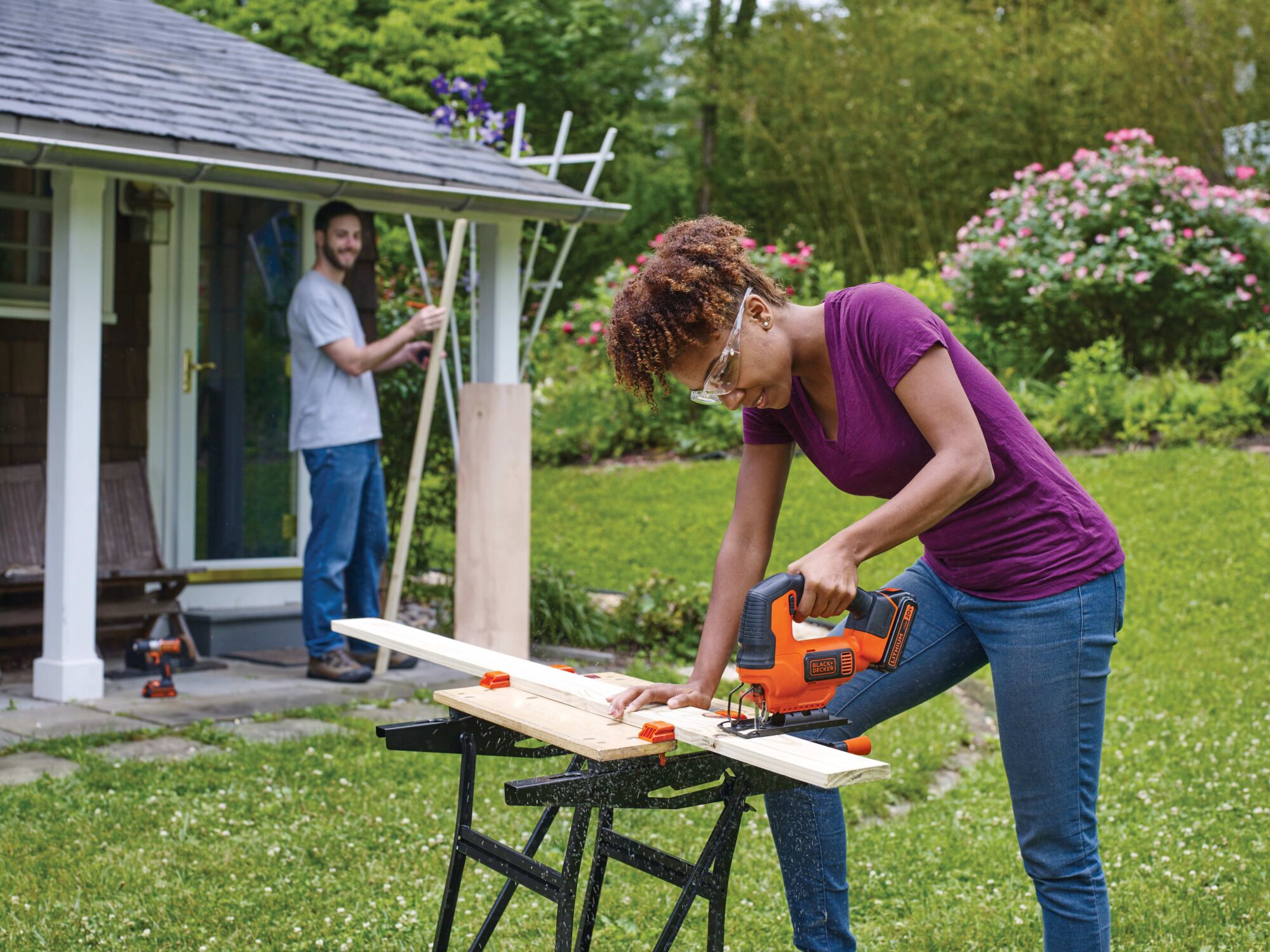 Cordless Jigsaw being used by person to cut plywood for a project in collaboration with another person in home garden environment.
