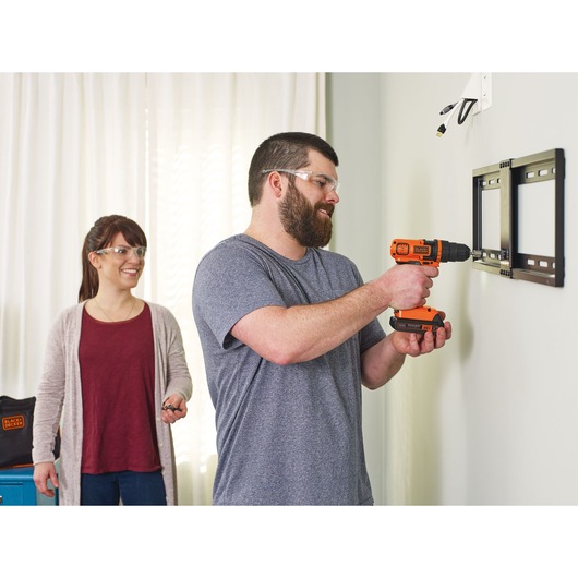 Lithium ion drill and driver plus 68 piece project kit being used to drill a tv frame into the wall by a person.